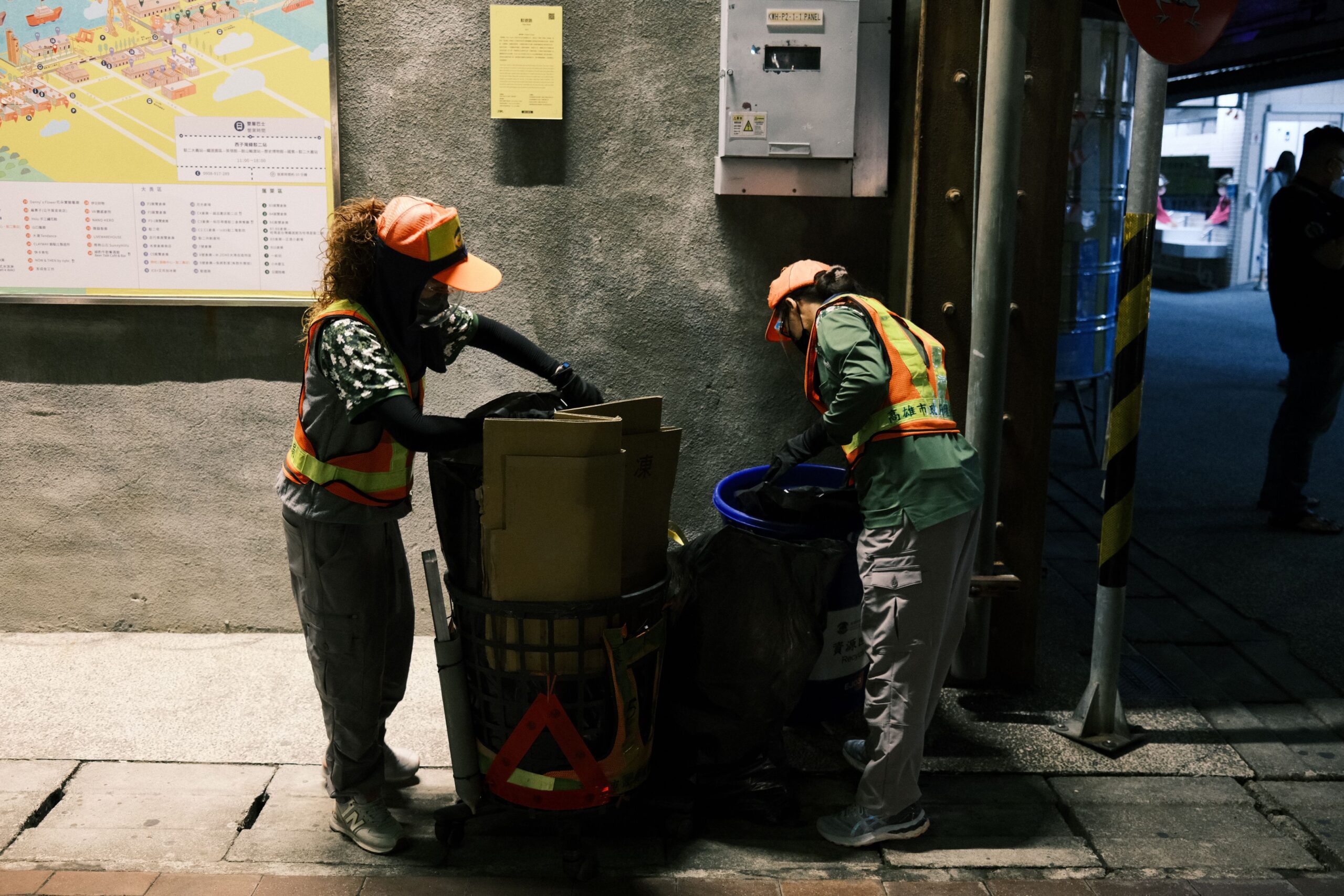 Two workers sorting trash on a dimly lit street in Kaohsiung, Taiwan.