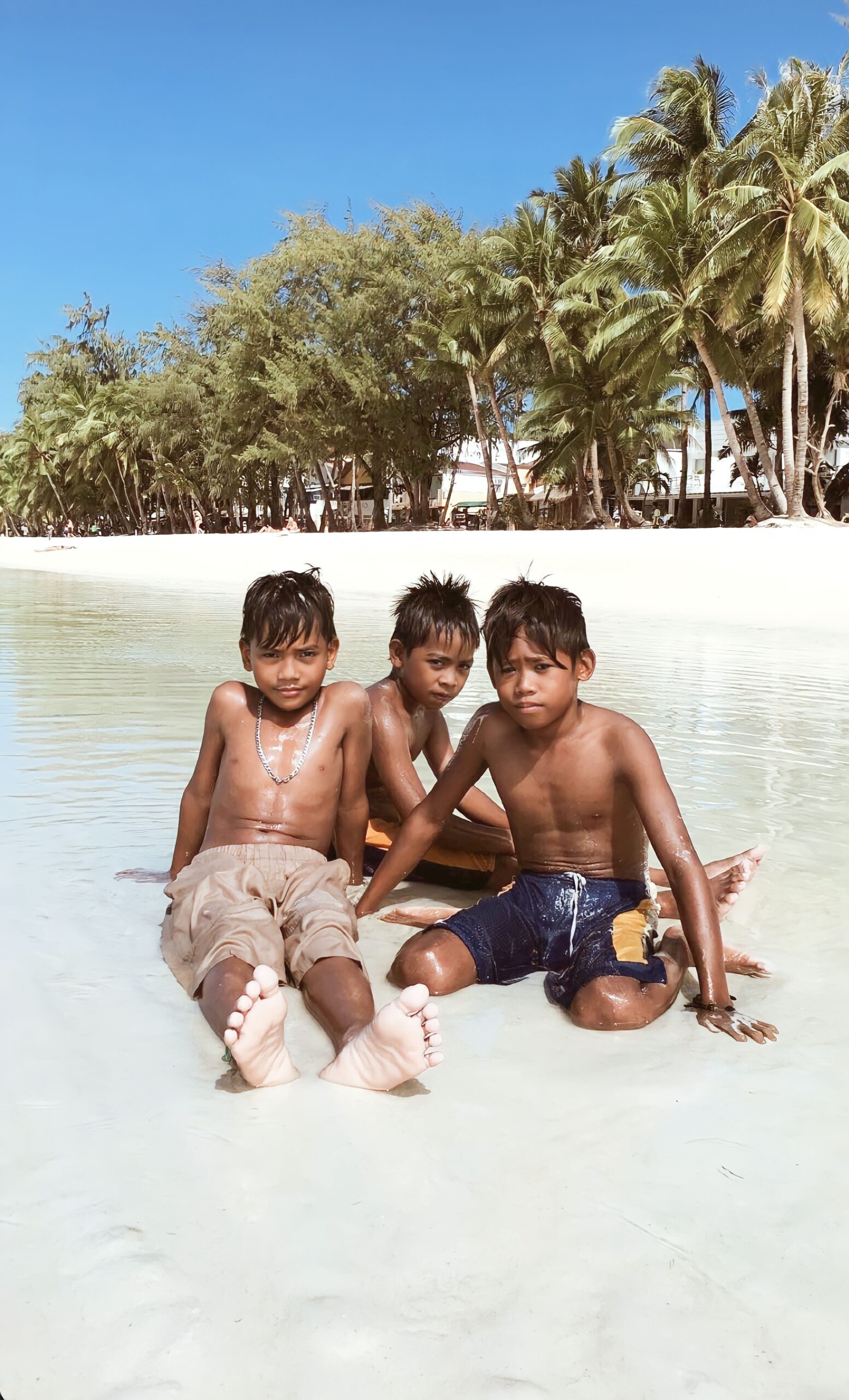 Three boys bask in the sun at a tropical beach in Malay, Philippines, showcasing carefree childhood moments.